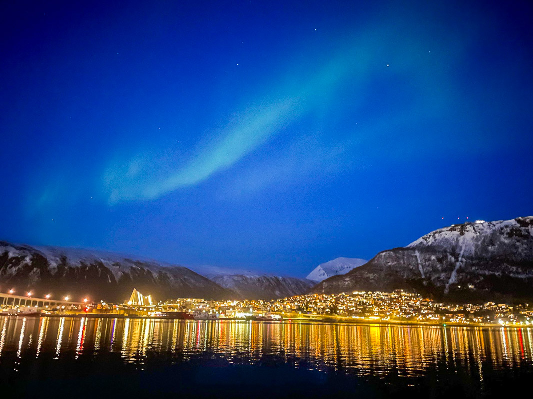 photograph: auora borealis; city lights by a large pool of water; rocks