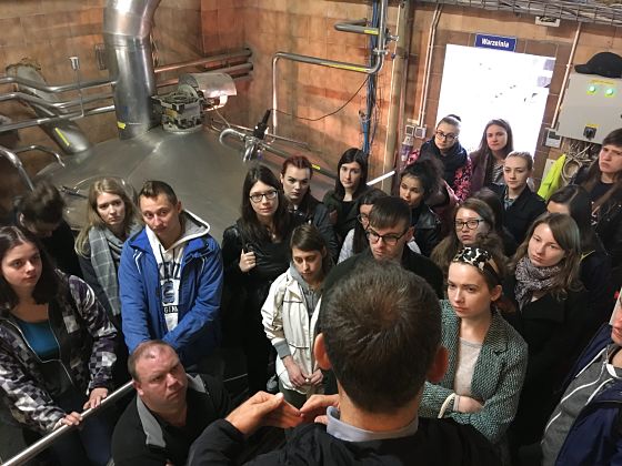 photograph: a group of more than ten people in a brewery hall, next to a kettle