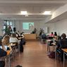 zdjęcie: kilkanaście osób w sali seminaryjnej, jedna mówi stojąc, pozostałe słuchają siedząc; w tle, na ekranie, slajd z prezentacją multimedialną
