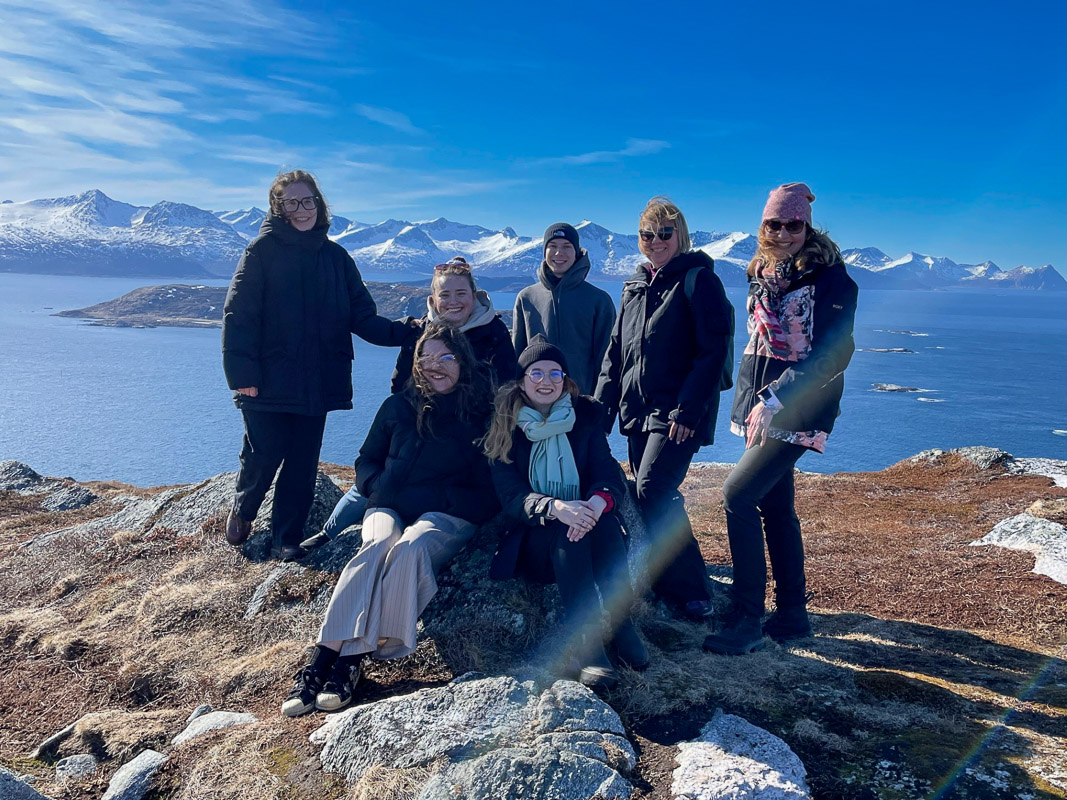 photograph: seven people by a rock; backround: a large pool of water, rocks, a blue sky