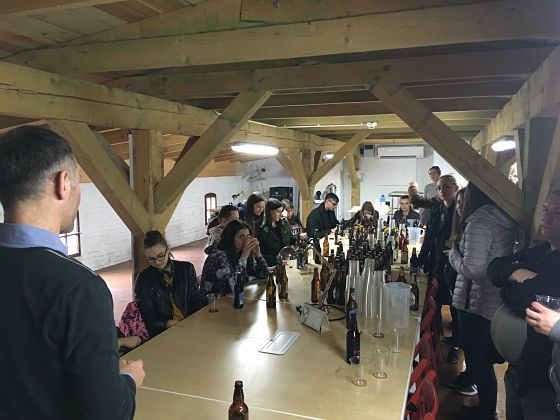 photograph: a group of more than ten people by a table with some glasses and bottles