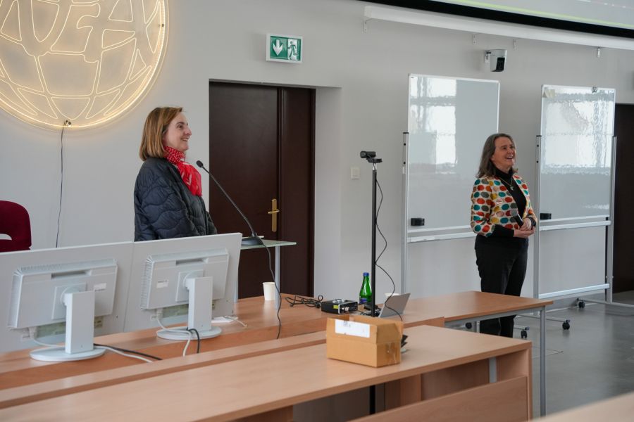 zdjęcie: osoba stoi w sali wykładowej; na ekranie za nią: obraz z rzutnika