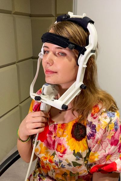 photograph: a person demonstrates the use of an ultrasound device; the head of the device is positioned under the person’s chin