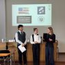 zdjęcie: trzy osoby stoją w sali seminaryjnej; w tle, na ekranie, slajd ze znakami biorących w wydarzeniu kół studenckich