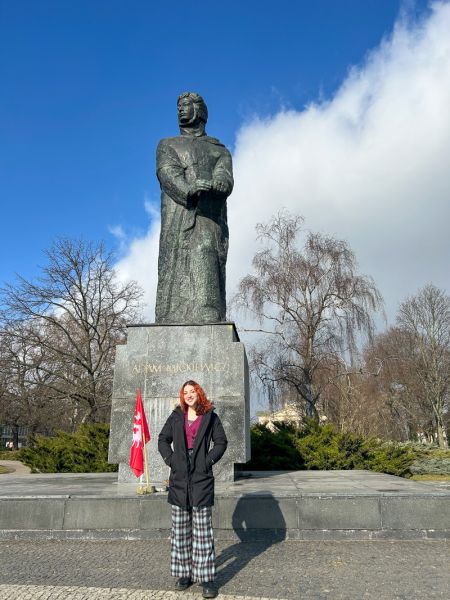 zdjęcie: osoba pozuje do zdjęcia przed pomnikiem przedstawiającym Adama Mickiewicza w Poznaniu