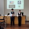zdjęcie: dwie osoby stoją w sali seminaryjnej; w tle, na ekranie, slajd ze znakami biorących w wydarzeniu kół studenckich