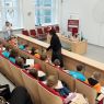 zdjęcie: sala wykładowa: wykładowca, trzymając w ręce mikrofon, stoi pośrodku grupy kilkudziesięciu dzieci oraz ich opekunów siedzących na sali