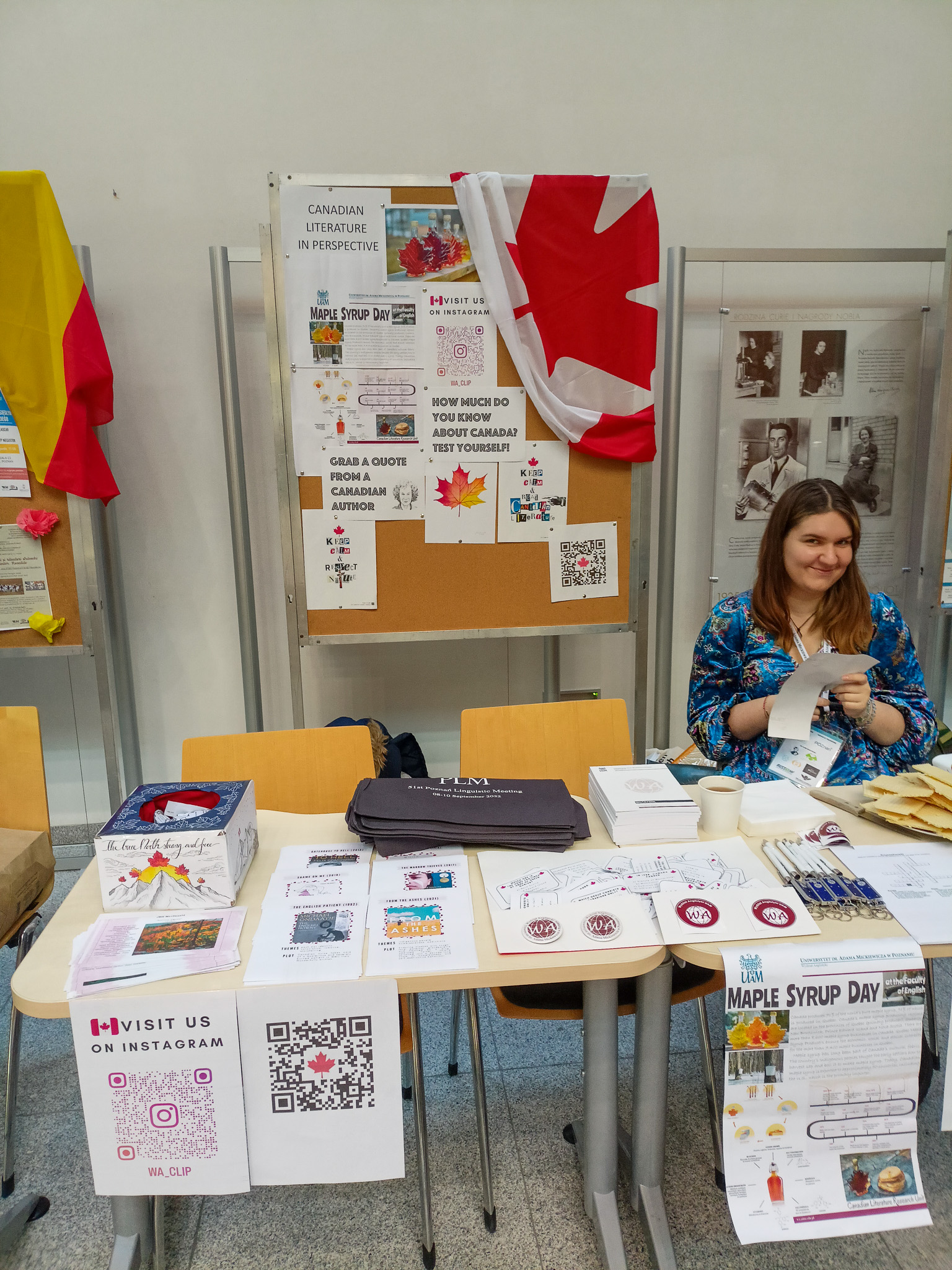 fotografia ilustrująca stoisko koła naukowego Canadian Literature in Perspective: jedna osoba siedząca za stołem, spoglądająca w stronę obiektywu